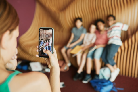 A person taking a picture on a smartphone of four people on a bench inside a building.